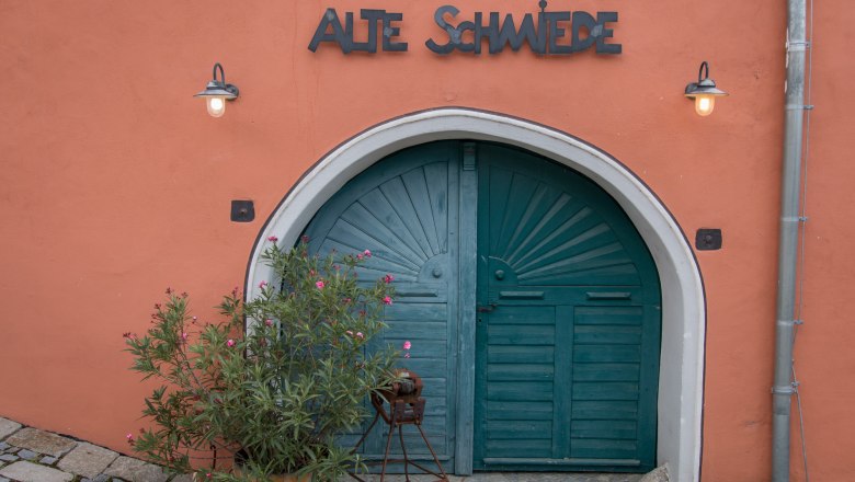 Das Alte Hof-Tor, © Alte Schmiede Schönberg Altes Tor mit der Aufschrift 'Alte Schmiede' und Pflanzen davor.