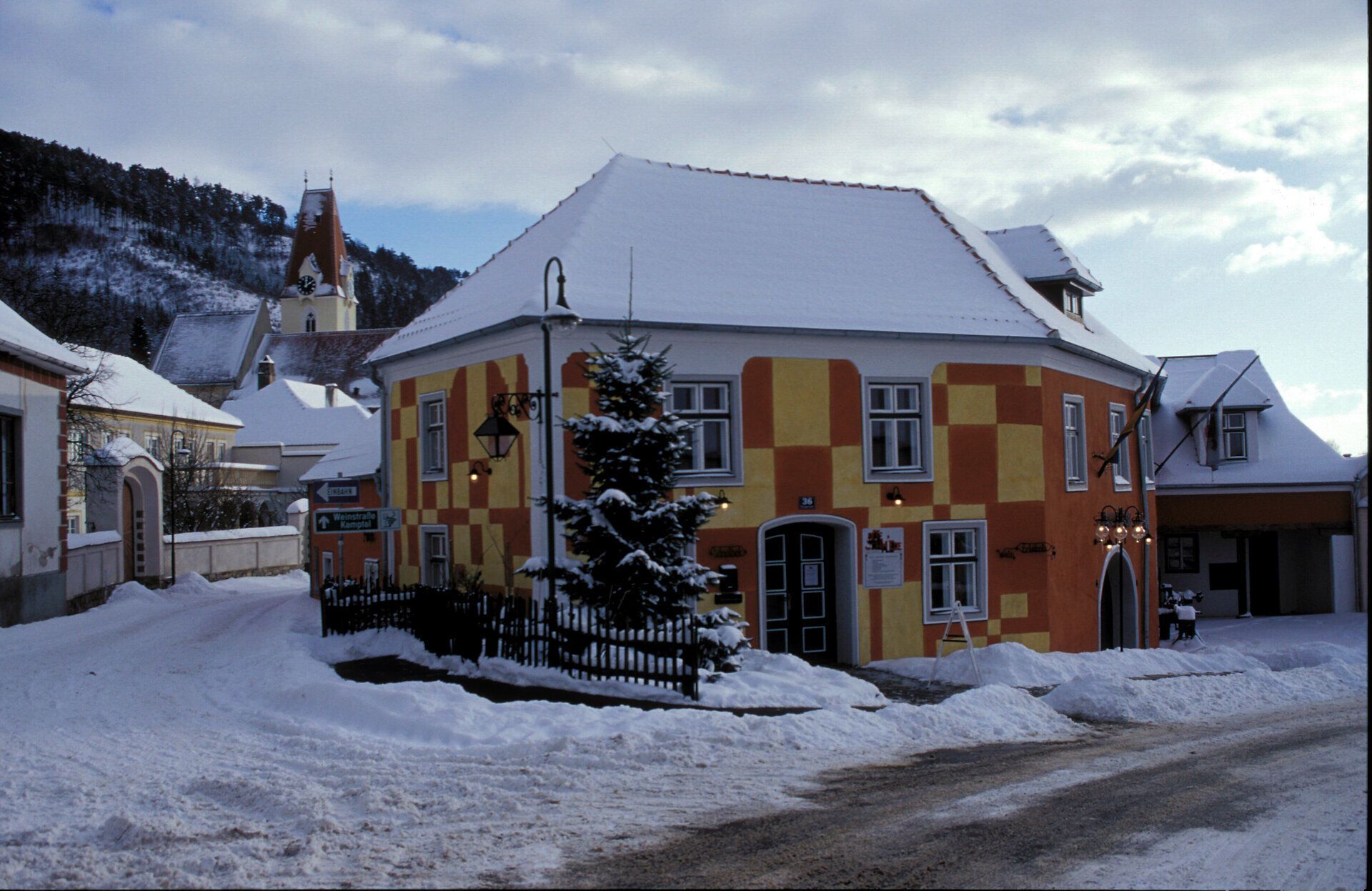 In einer malerischen Winterlandschaft, wo die schneebedeckten Dächer der bunten Häuser sanft im Licht der tiefstehenden Sonne glitzern, entfaltet sich eine zauberhafte Ruhe. Die verschneiten Straßen laden zu einem gemütlichen Spaziergang ein, während die frische, klare Luft die Sinne belebt.