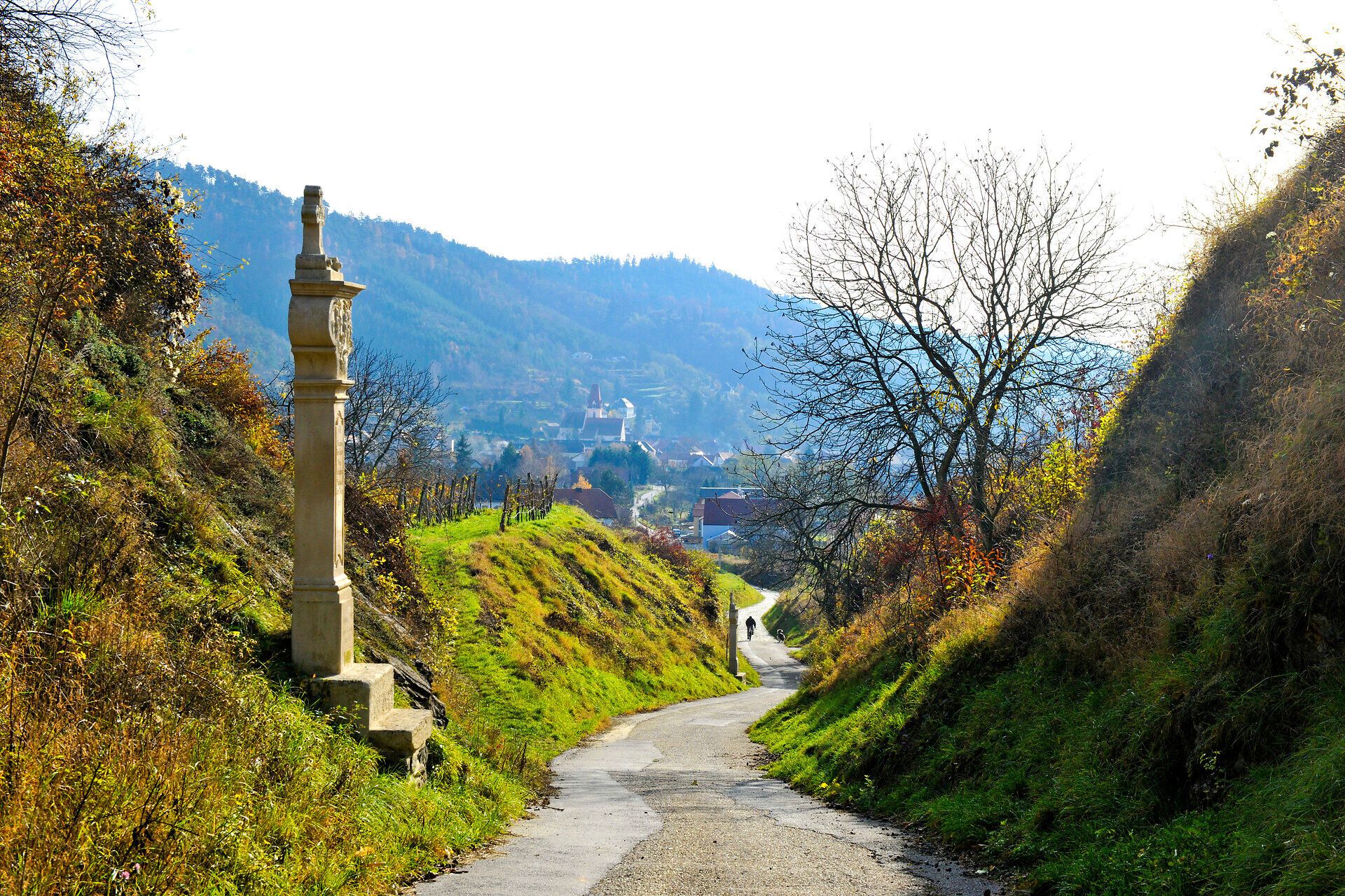 Ein sanfter Weg schlängelt sich durch die malerische Landschaft, umgeben von sanften Hügeln und üppigem Grün. Die warmen Sonnenstrahlen tauchen die Szenerie in ein goldenes Licht und laden dazu ein, die Ruhe und Schönheit der Natur zu genießen.