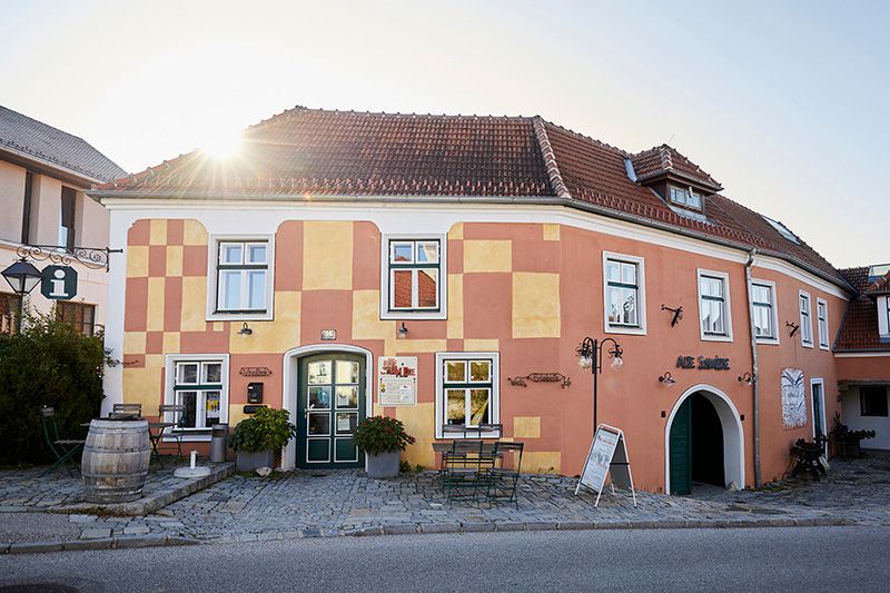 Historisches Gebäude mit gelber und roter Fassade, Sonnenschein im Hintergrund.