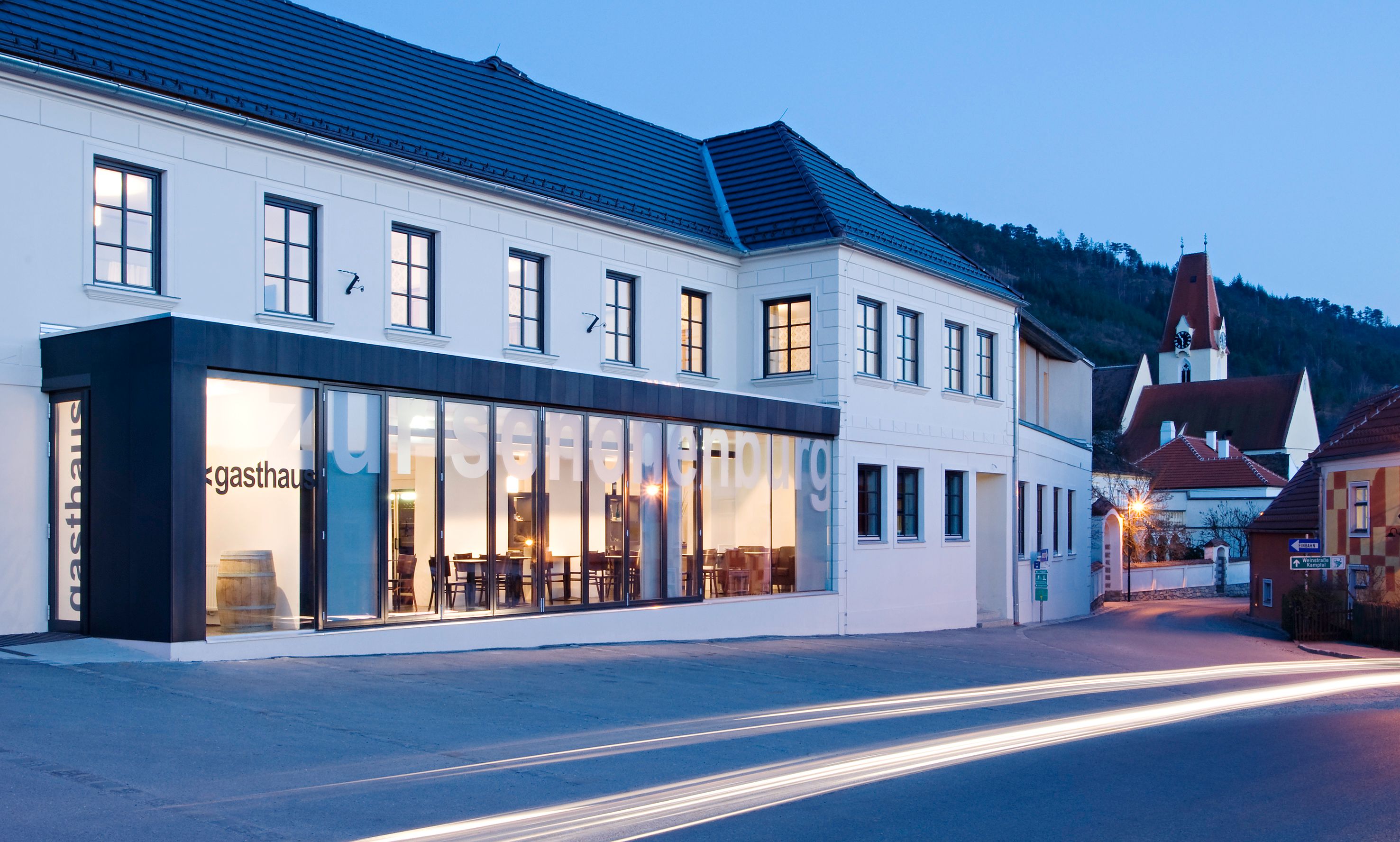 Außenansicht des Gasthofs Hotel Zur Schonenburg bei Dämmerung mit beleuchteten Fenstern und vorbeifahrenden Autos.
